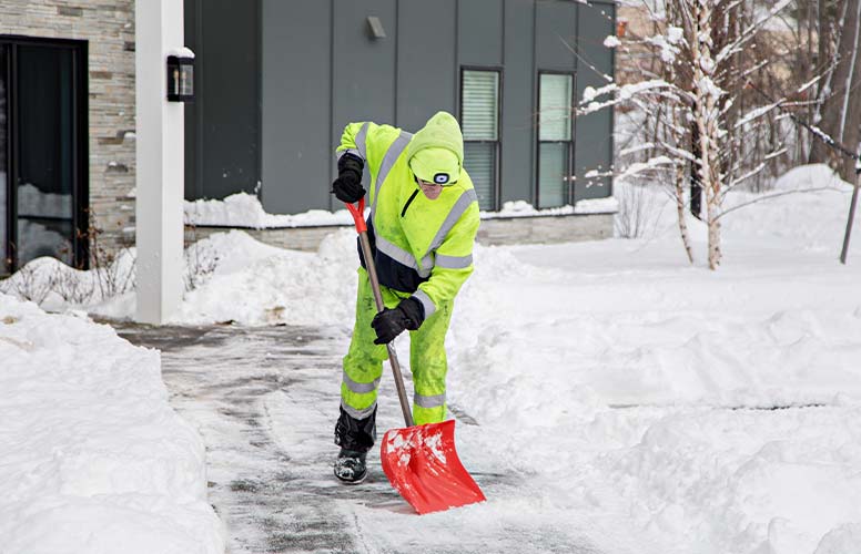 Man shoveling walkway with high visibility clothing.